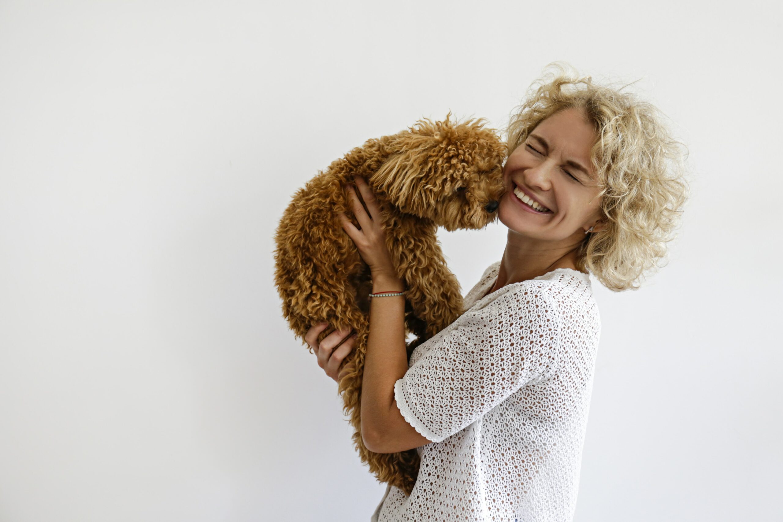 A smiling person holds their beloved curly-haired dog close to their face against a plain background, celebrating the importance of spaying and neutering for a healthier pet community.