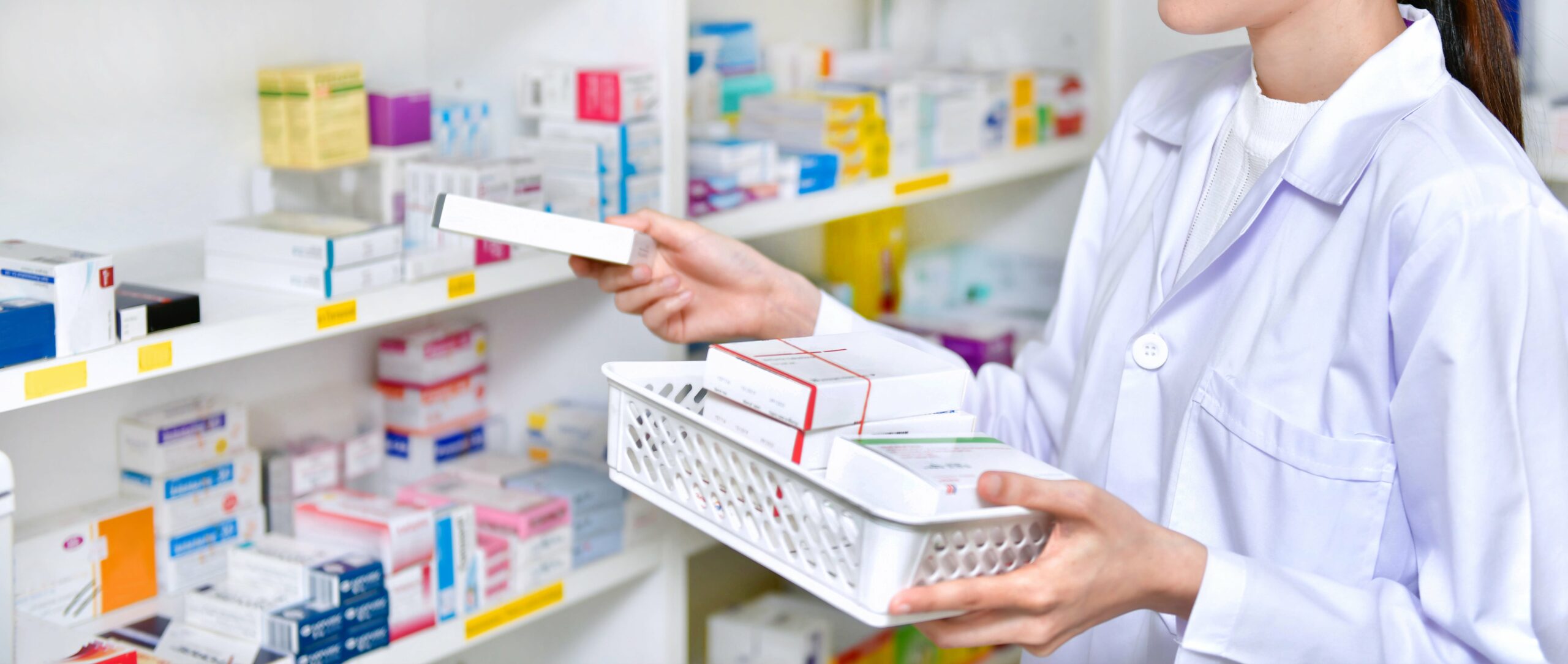 A pharmacist in a white coat navigates the pharmacy aisles, skillfully selecting medication boxes from the shelves and placing them into a basket.